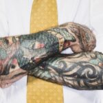 Brazos cruzados, tapados casi en su totalidad por tatuajes; la persona viste camisa y corbata.
